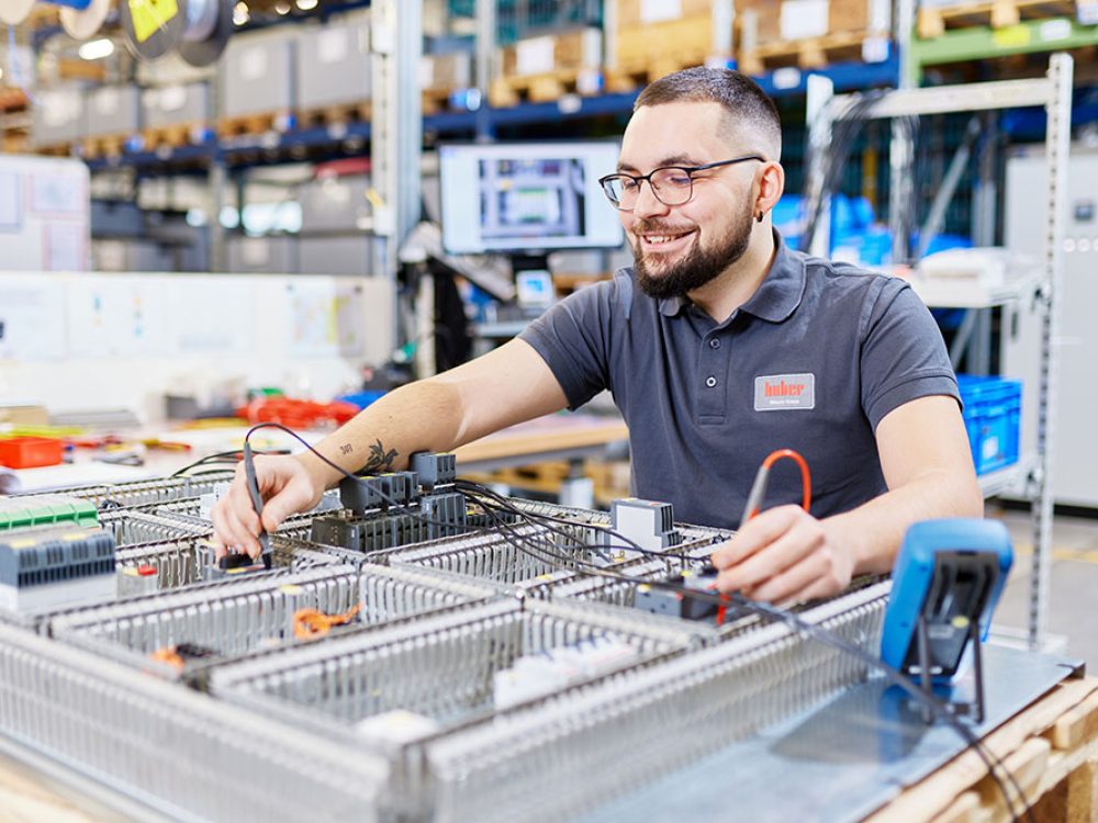 Ein junger Mann arbeitet in einer industriellen Werkstatt und überprüft elektronische Schaltkreise auf einem Tisch