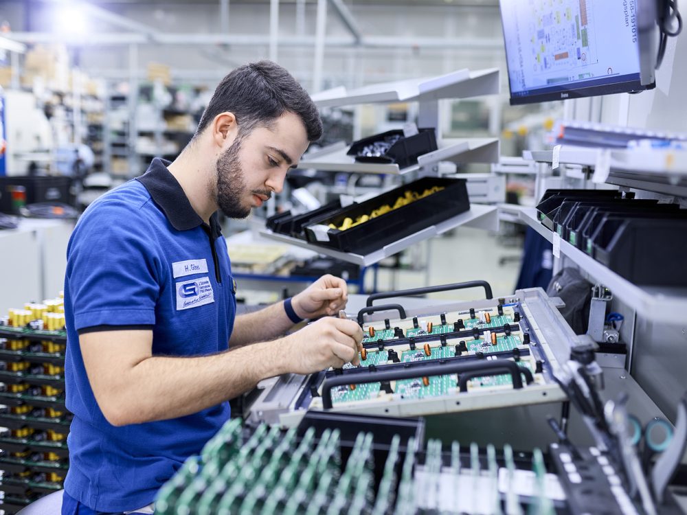 J. Schneider Elektrotechnik Azubi arbeitet an einer Montage-Station in einer Fabrik