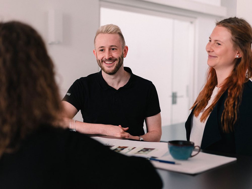 Besprechung zwischen zwei Frauen und einem Mann, die an einem Stehtisch stehen.
