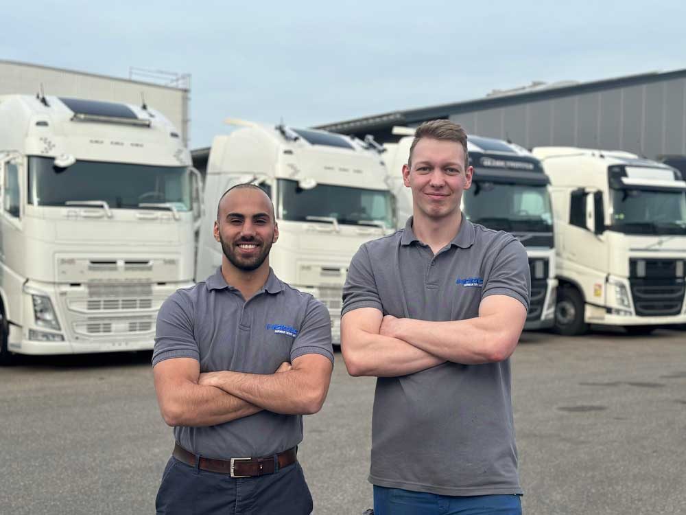 Männliche Azubis stehen mit verschränkten Armen vor vier LKWs