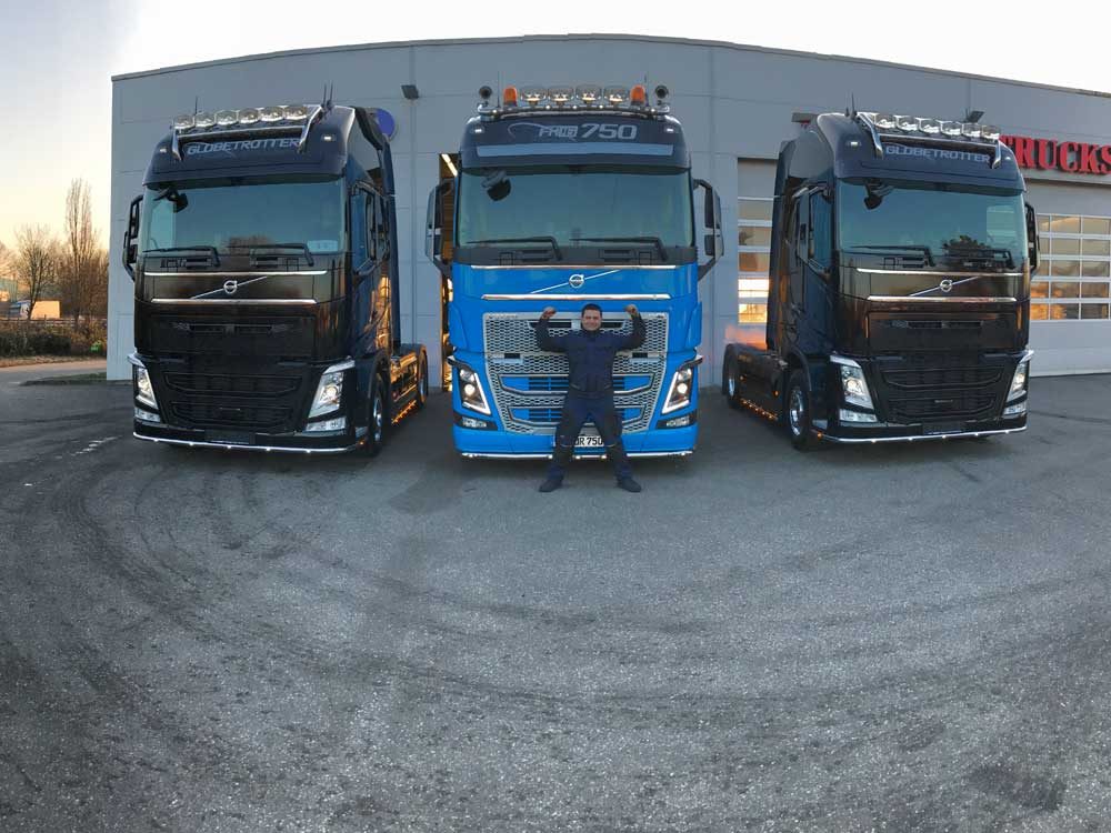 Ein Mann steht mit ausgebreiteten Armen zwischen drei großen Lastwagen.